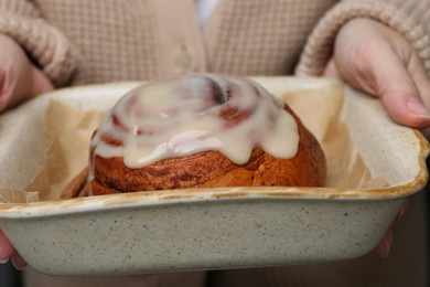 Photo of Woman holding baking dish with tasty cinnamon roll, closeup