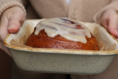 Photo of Woman holding baking dish with tasty cinnamon roll, closeup