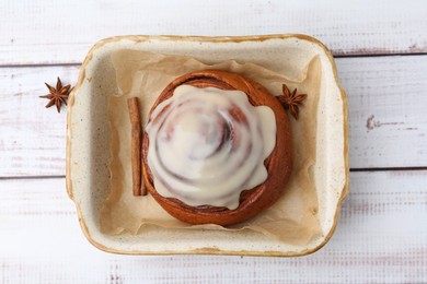 Photo of Tasty cinnamon roll with cream and spices in baking dish on white wooden table, top view