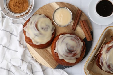 Photo of Tasty cinnamon rolls with cream, spices and coffee on white tiled table, flat lay