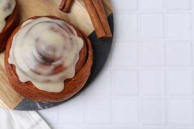 Photo of Tasty cinnamon roll with cream and spices on white tiled table, top view. Space for text