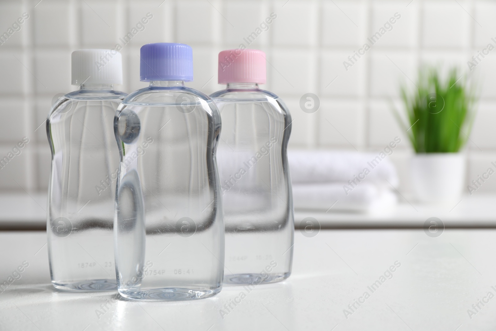 Photo of Baby oil in bottles on white table against blurred background. Space for text