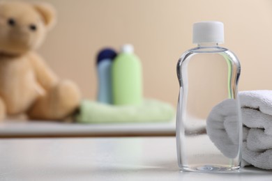 Photo of Baby oil in bottle and towel on white table against blurred background. Space for text