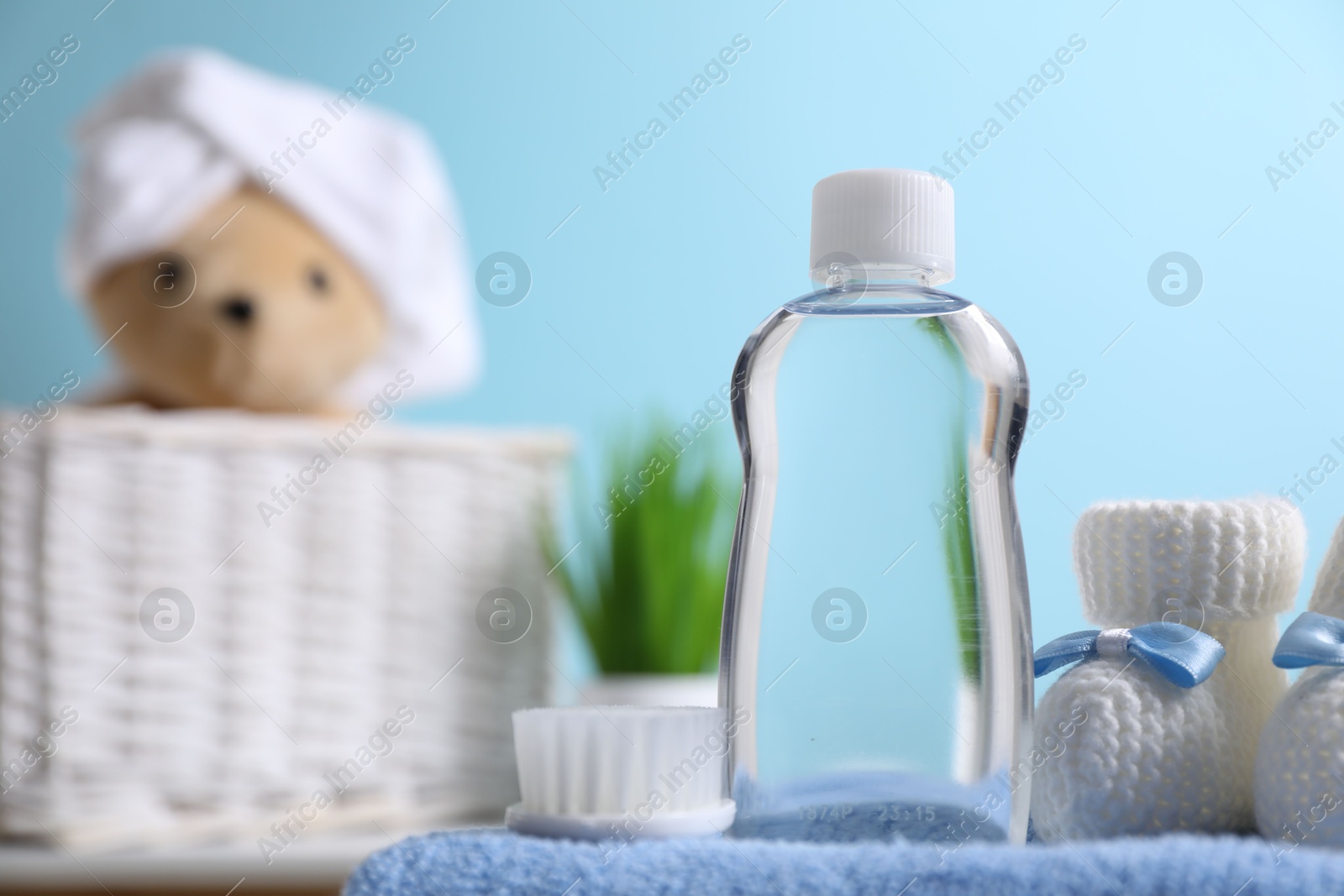 Photo of Baby oil in bottle, booties and brush on towel against blurred background