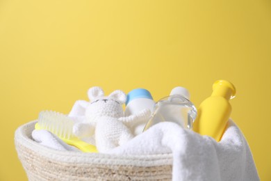 Photo of Baby oil and other toiletries in basket against yellow background, closeup. Space for text