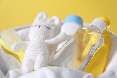 Photo of Baby oil and other toiletries in basket against yellow background, closeup