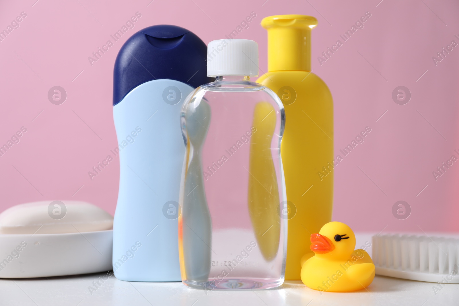 Photo of Baby oil and other toiletries on white table against pink background