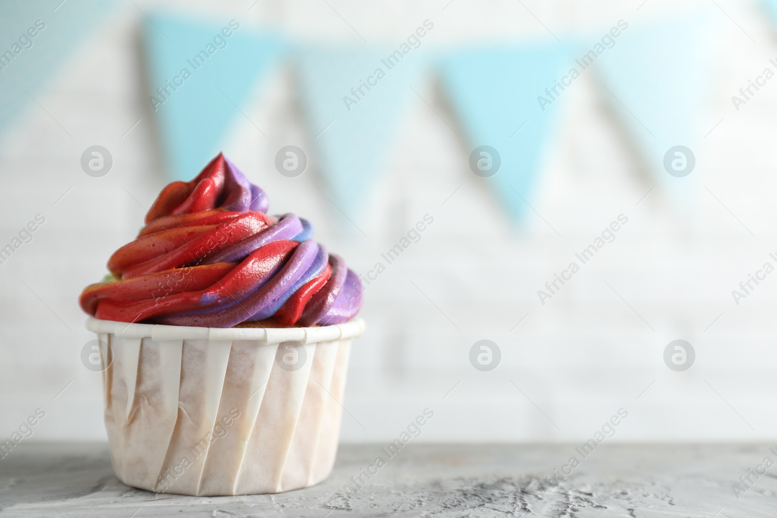 Photo of Delicious cupcake with colorful cream on grey textured table against blurred background, closeup. Space for text