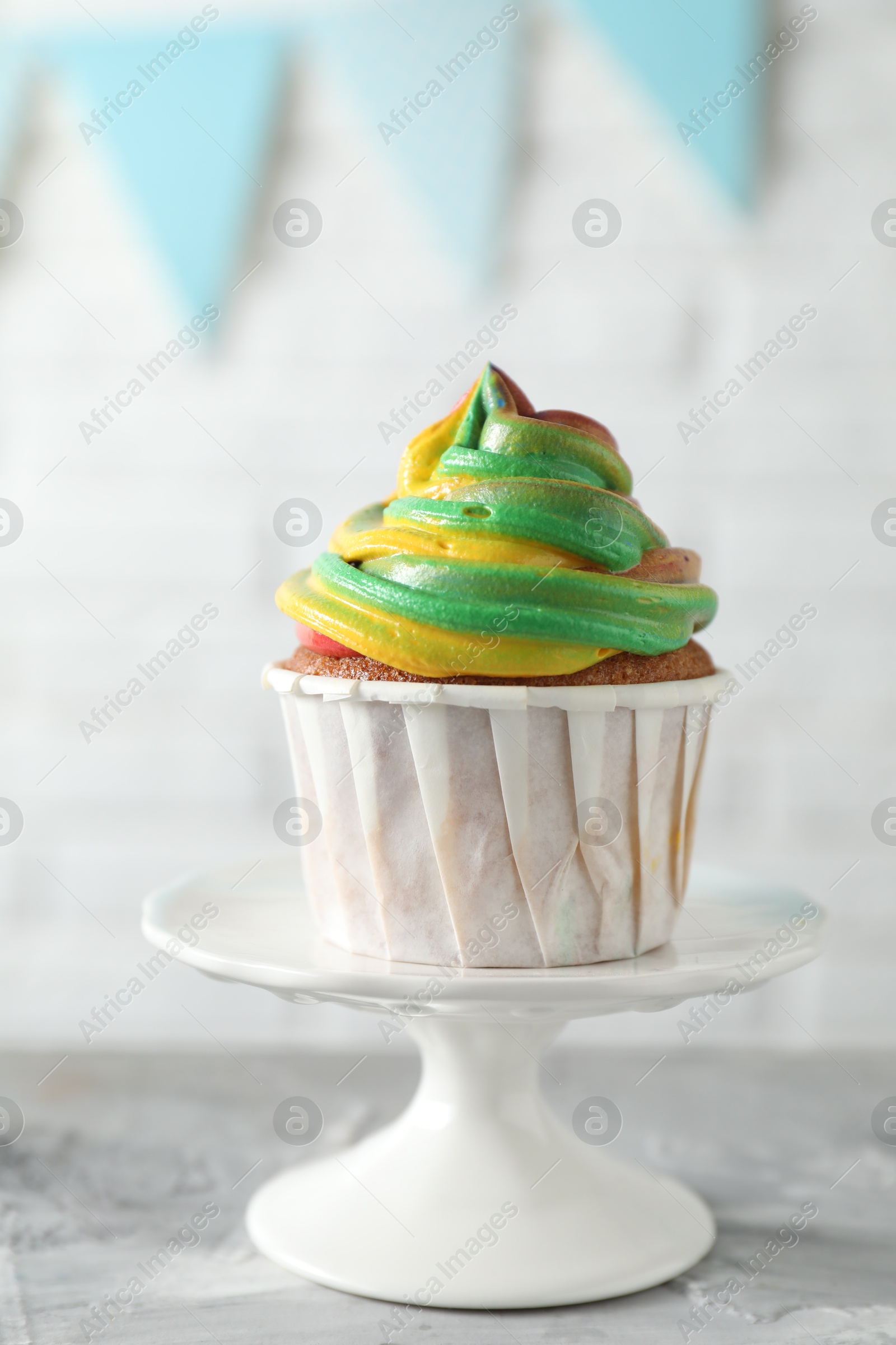 Photo of Delicious cupcake with colorful cream on grey textured table against blurred background, closeup