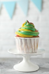 Photo of Delicious cupcake with colorful cream on grey textured table against blurred background, closeup