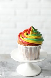 Photo of Delicious cupcake with colorful cream on grey textured table against blurred background, closeup