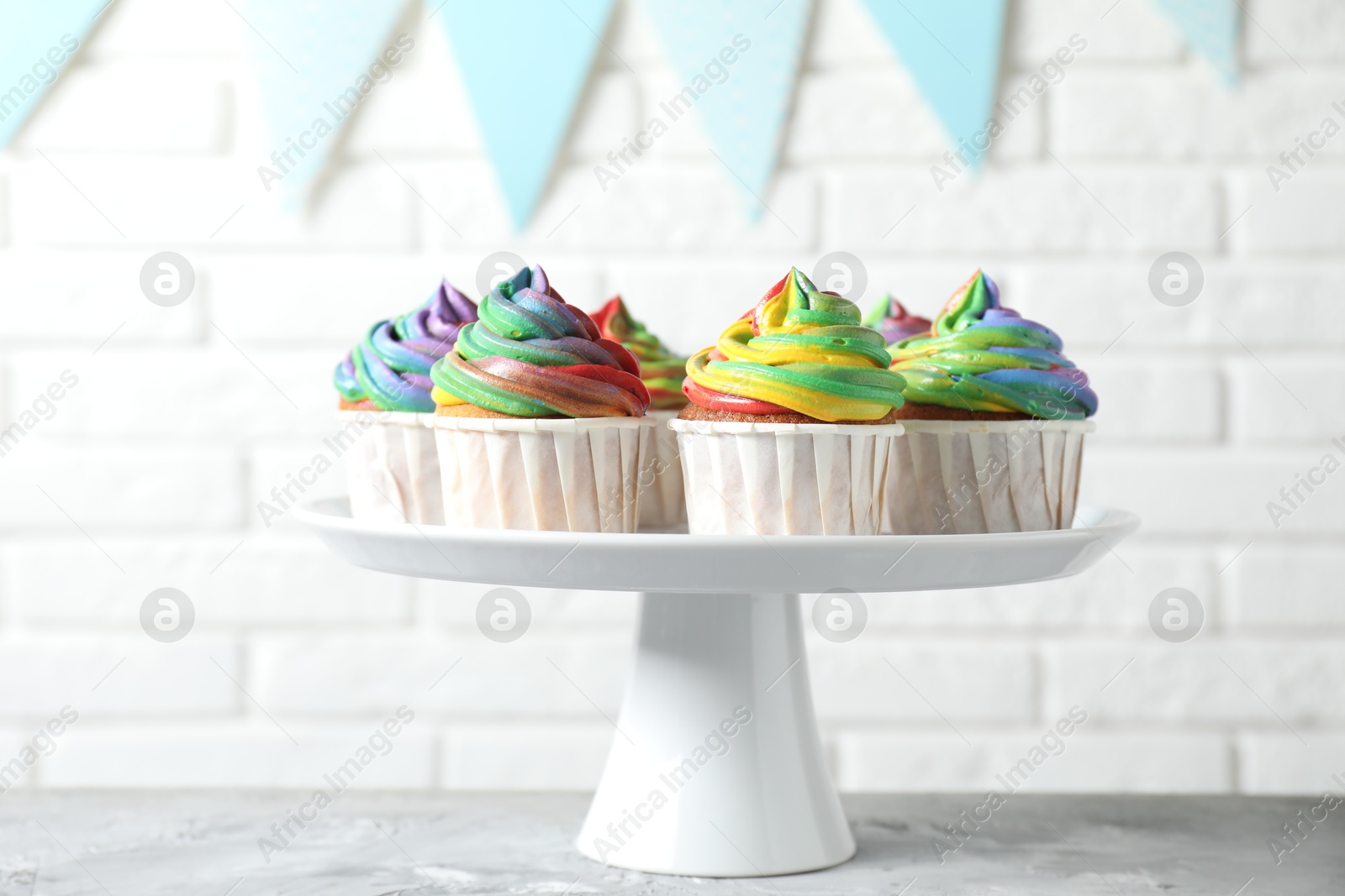 Photo of Delicious cupcakes with colorful cream on grey textured table near white brick wall, closeup