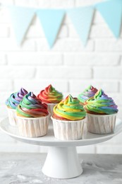 Photo of Delicious cupcakes with colorful cream on grey textured table near white brick wall, closeup. Space for text