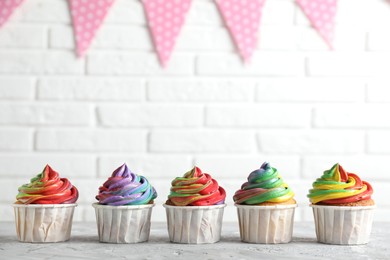 Photo of Delicious cupcakes with colorful cream on grey textured table near white brick wall, closeup. Space for text