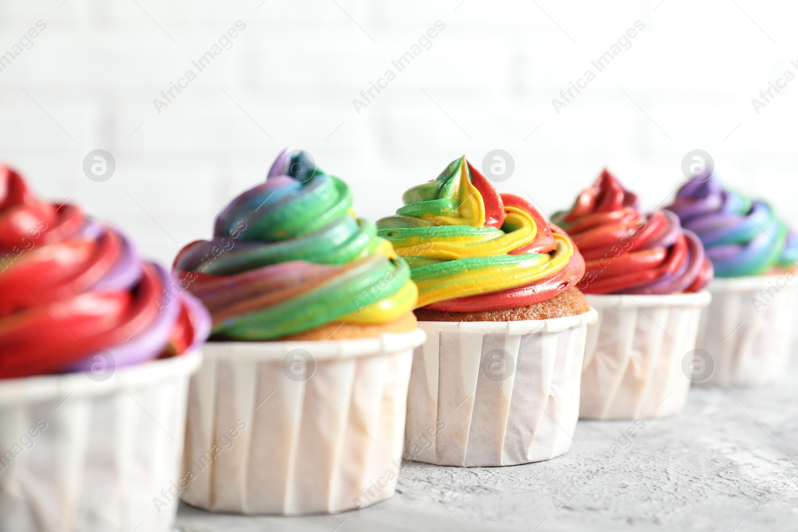 Photo of Delicious cupcakes with colorful cream on grey textured table near white wall, closeup