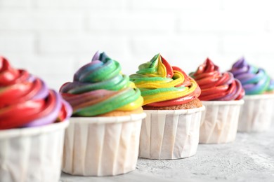 Photo of Delicious cupcakes with colorful cream on grey textured table near white wall, closeup