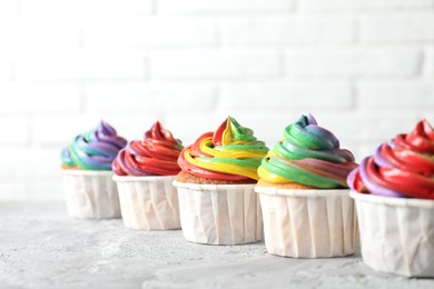 Photo of Delicious cupcakes with colorful cream on grey textured table near white wall, closeup