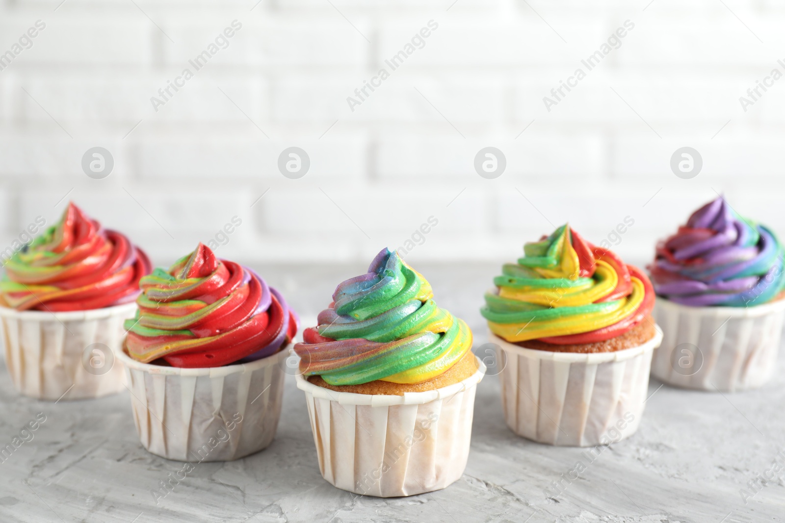 Photo of Delicious cupcakes with colorful cream on grey textured table near white wall, closeup. Space for text