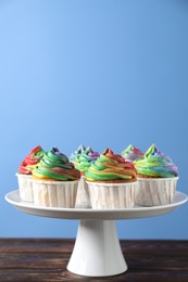 Photo of Delicious cupcakes with colorful cream on wooden table against blue background, closeup. Space for text