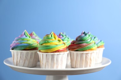 Photo of Delicious cupcakes with colorful cream on stand against blue background, closeup