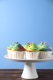 Photo of Delicious cupcakes with colorful cream on wooden table against blue background, closeup. Space for text