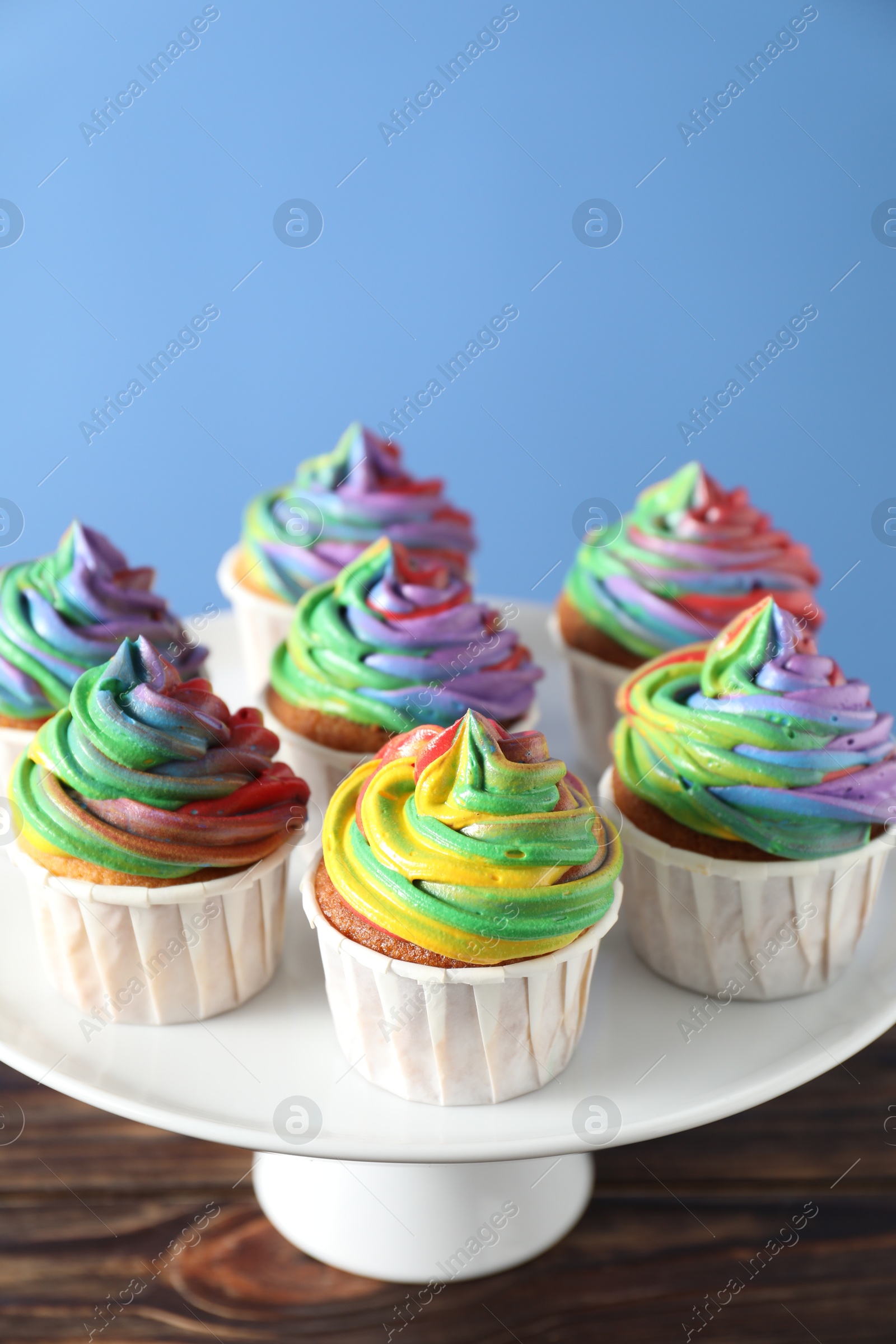 Photo of Delicious cupcakes with colorful cream on wooden table against blue background, closeup