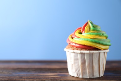 Photo of Delicious cupcake with colorful cream on wooden table against blue background, closeup. Space for text