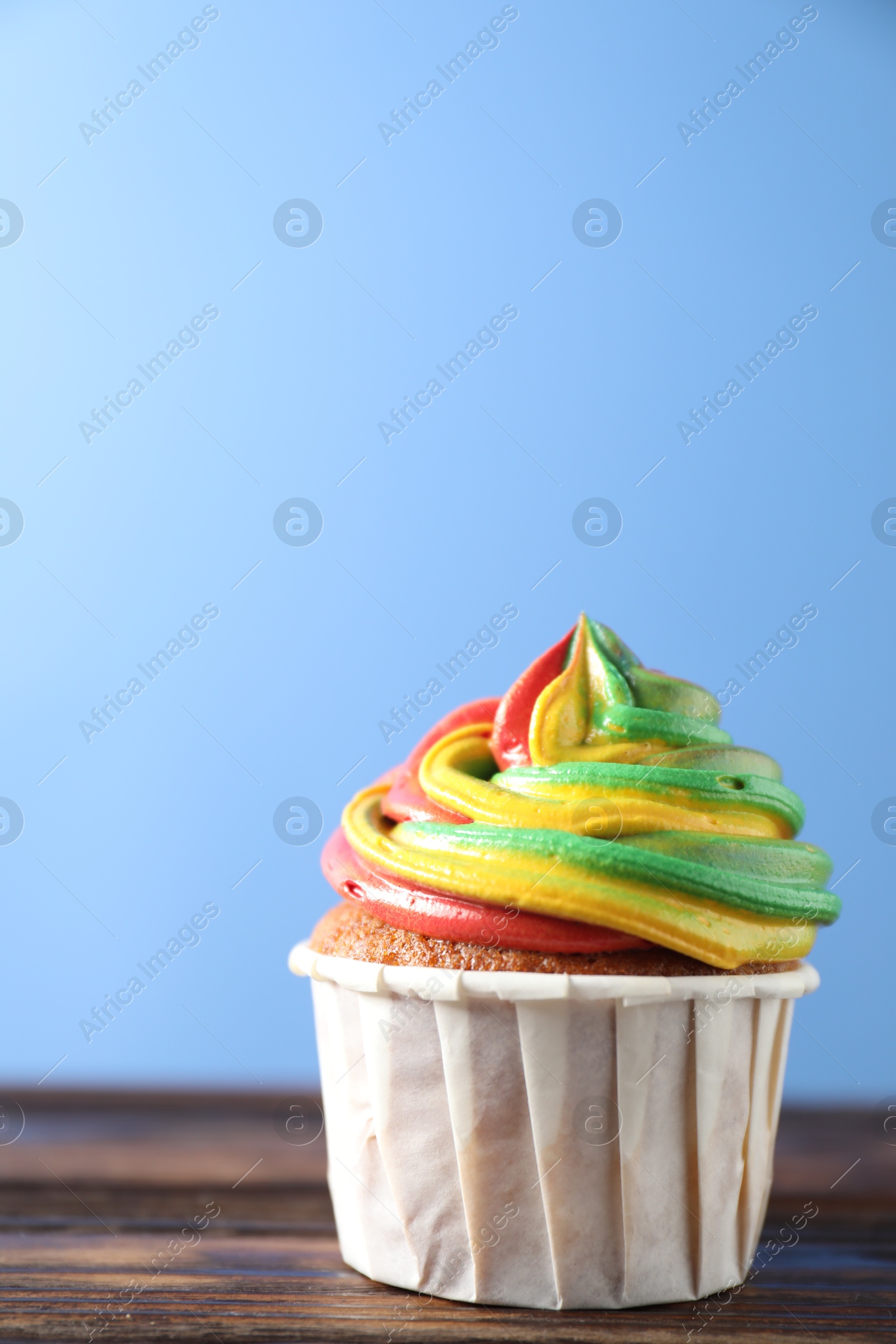 Photo of Delicious cupcake with colorful cream on wooden table against blue background, closeup. Space for text