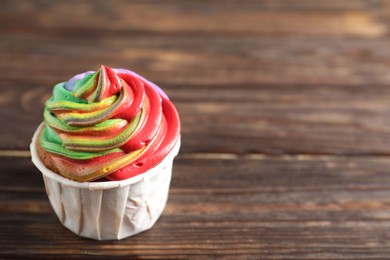 Photo of Delicious cupcake with colorful cream on wooden table, closeup. Space for text