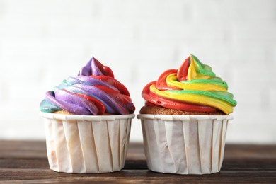 Photo of Delicious cupcakes with colorful cream on wooden table against white background, closeup