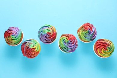 Photo of Delicious cupcakes with colorful cream on light blue background, flat lay