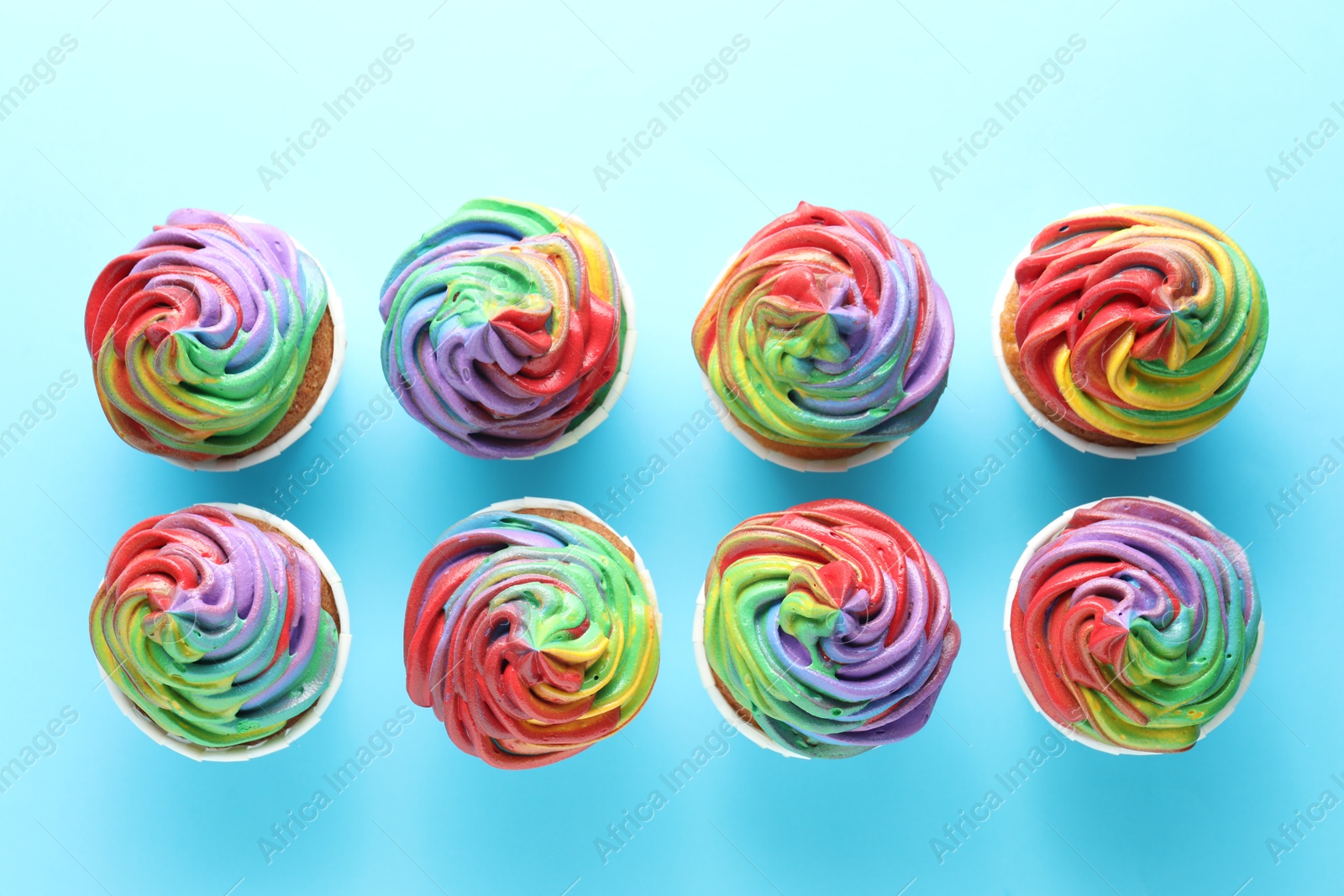 Photo of Delicious cupcakes with colorful cream on light blue background, flat lay