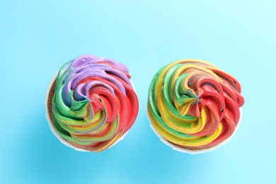 Photo of Delicious cupcakes with colorful cream on light blue background, flat lay