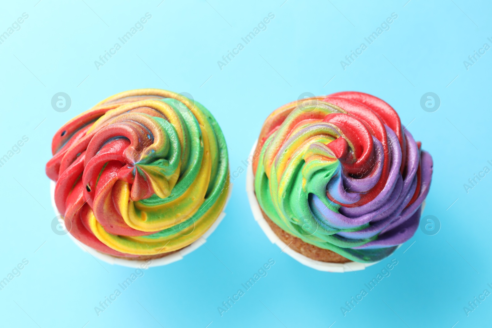 Photo of Delicious cupcakes with colorful cream on light blue background, flat lay