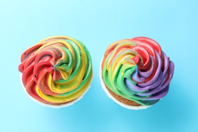 Photo of Delicious cupcakes with colorful cream on light blue background, flat lay