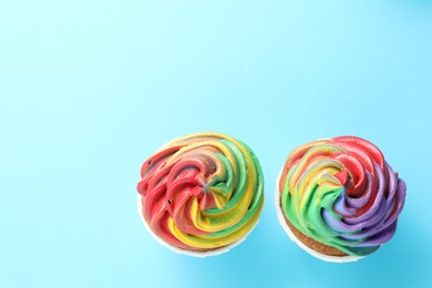 Photo of Delicious cupcakes with colorful cream on light blue background, flat lay. Space for text