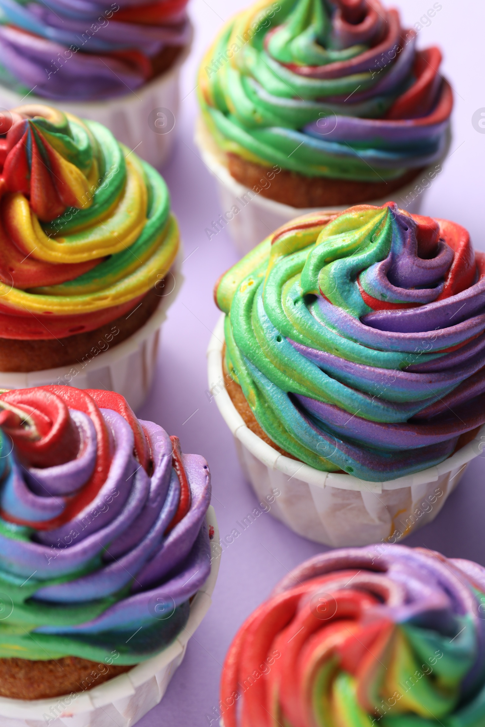 Photo of Delicious cupcakes with colorful cream on violet background, closeup