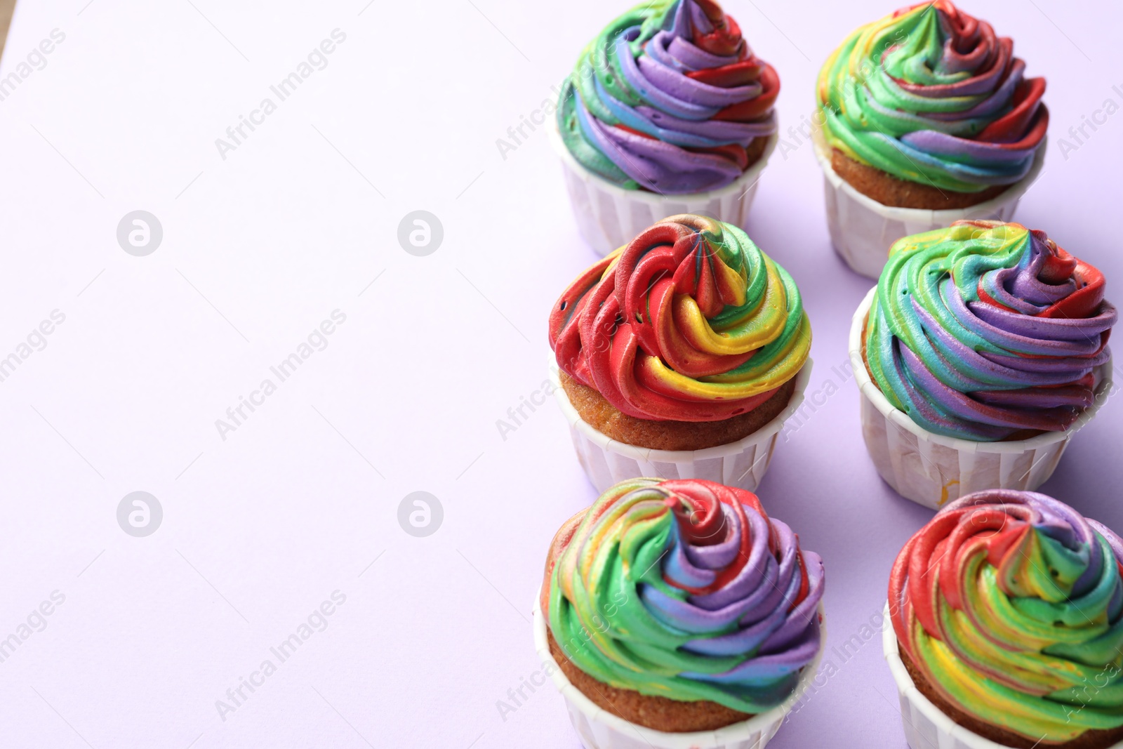 Photo of Delicious cupcakes with colorful cream on violet background, closeup. Space for text