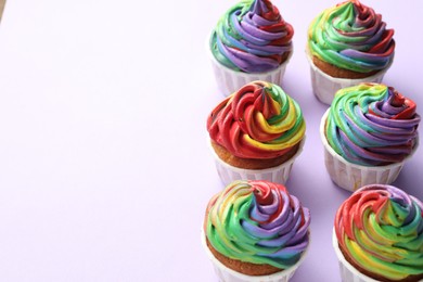 Photo of Delicious cupcakes with colorful cream on violet background, closeup. Space for text