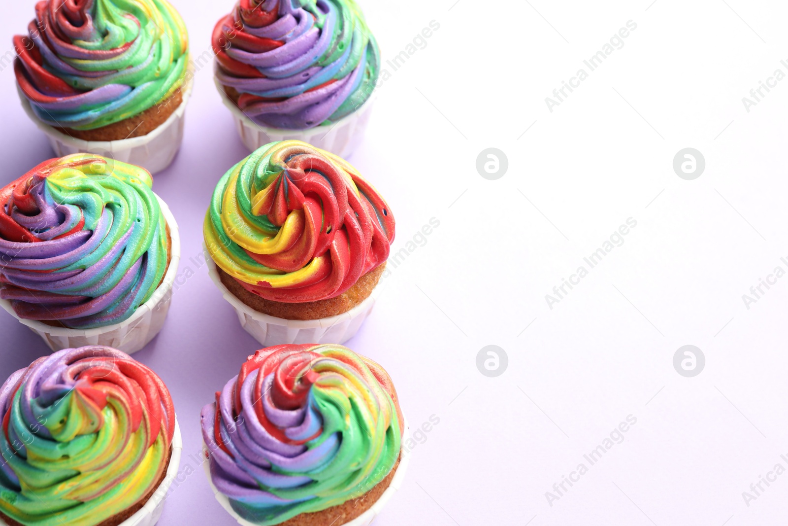 Photo of Delicious cupcakes with colorful cream on violet background. Space for text