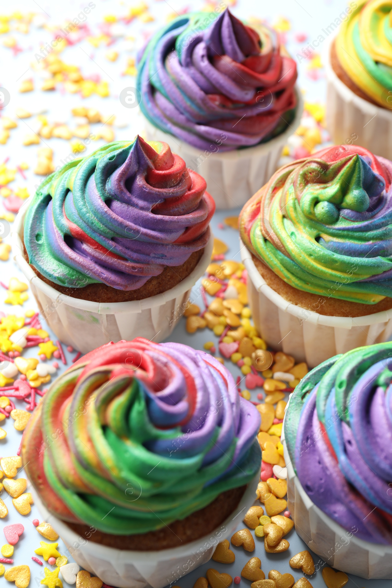 Photo of Delicious cupcakes with colorful cream and confetti on light table, closeup