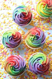 Photo of Delicious cupcakes with colorful cream and confetti on light table, flat lay