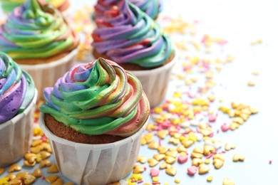 Delicious cupcakes with colorful cream and confetti on light table, closeup. Space for text