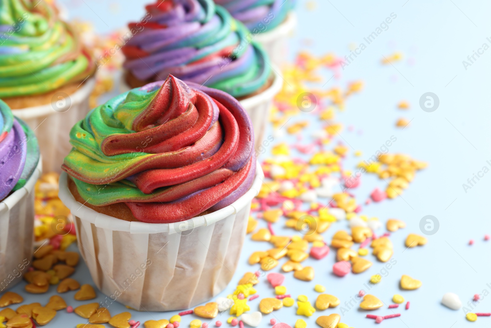 Photo of Delicious cupcakes with colorful cream and confetti on light table, closeup. Space for text