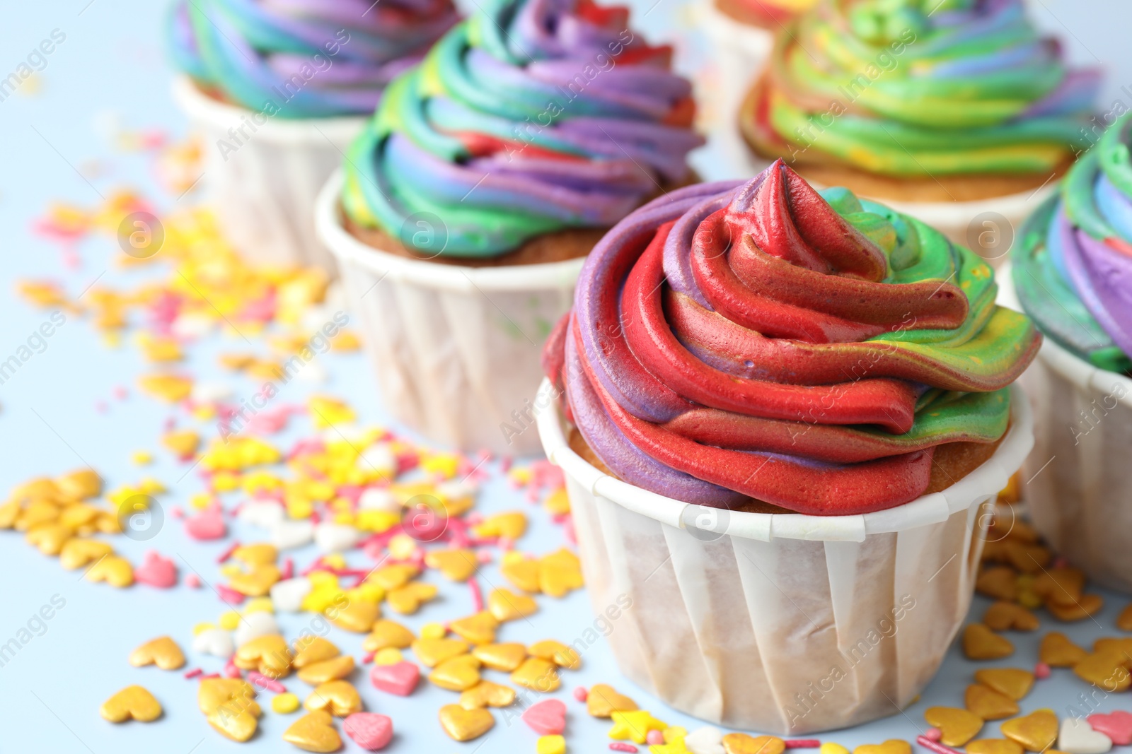 Photo of Delicious cupcakes with colorful cream and confetti on light table, closeup