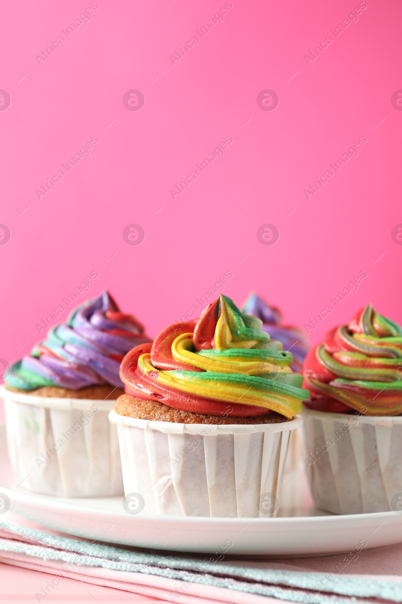 Photo of Delicious cupcakes with colorful cream on pink table, closeup. Space for text