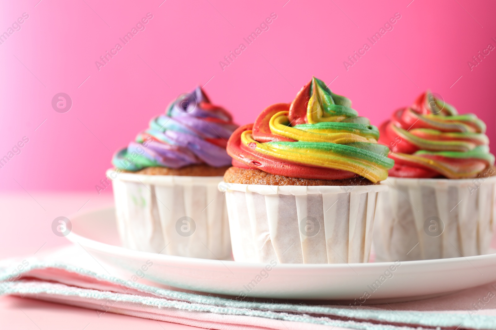 Photo of Delicious cupcakes with colorful cream on pink table, closeup