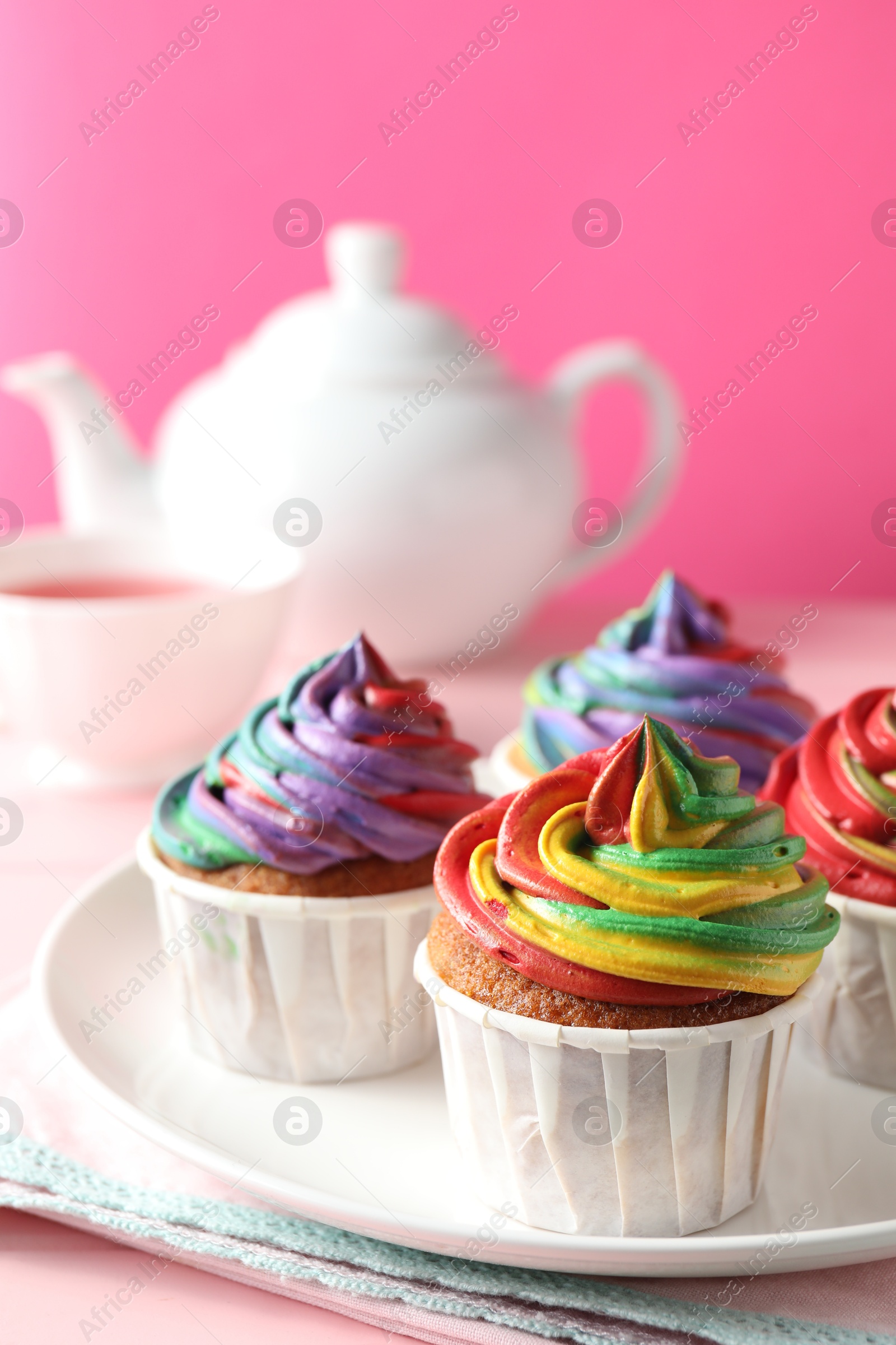 Photo of Delicious cupcakes with colorful cream and tea on pink table, closeup