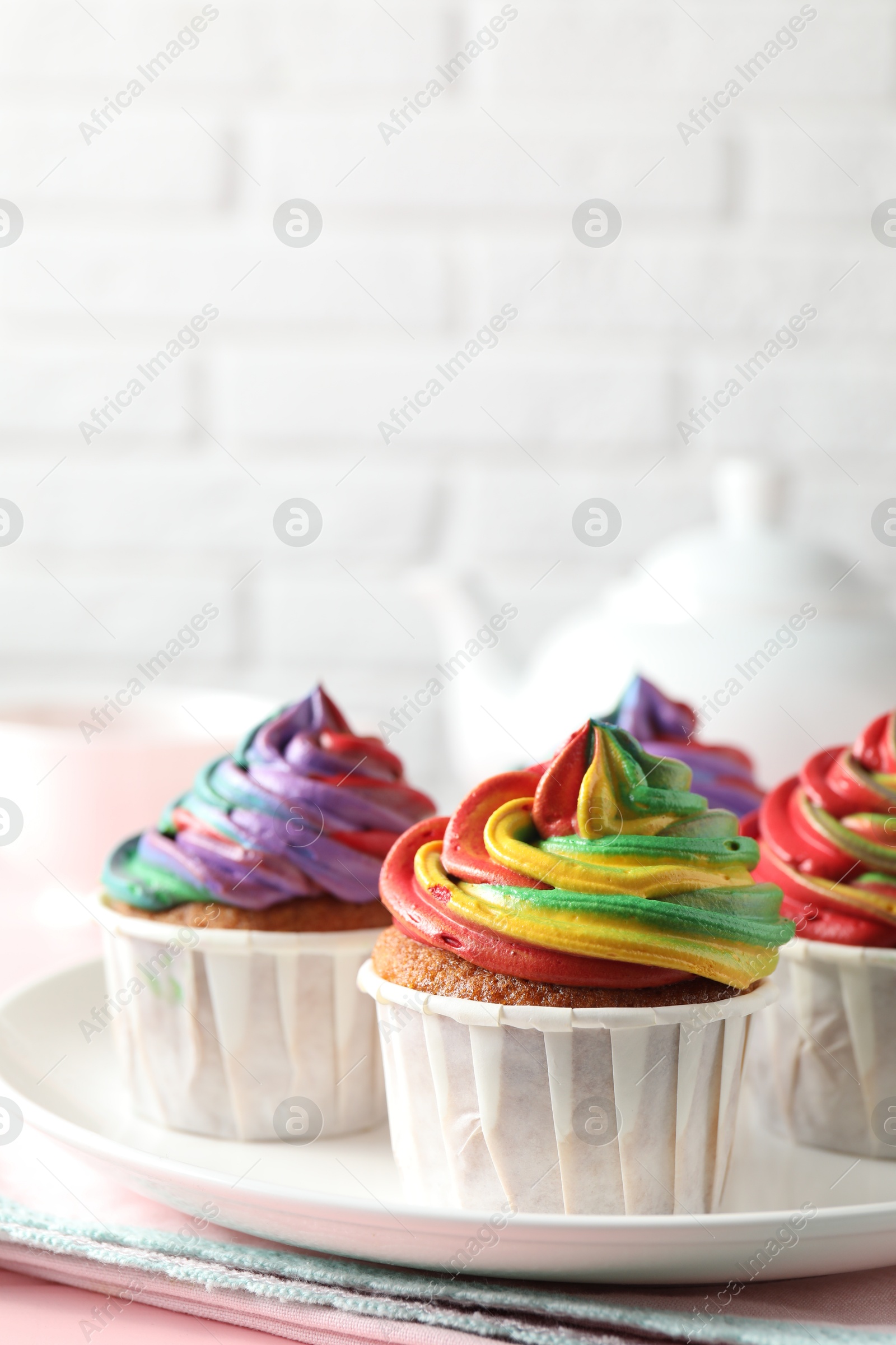 Photo of Delicious cupcakes with colorful cream and tea on pink table, closeup. Space for text