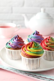 Photo of Delicious cupcakes with colorful cream and tea on pink table, closeup